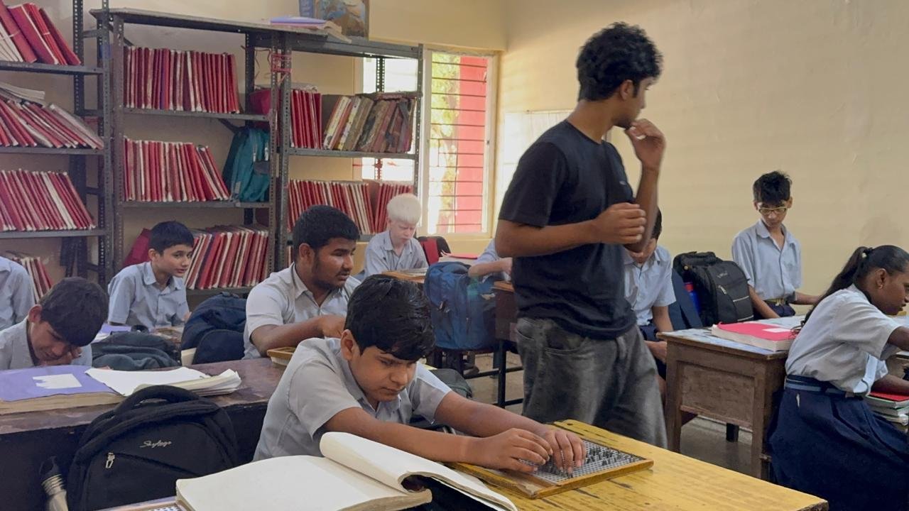 A student writing on a braille slate at his desk while I speak with the class