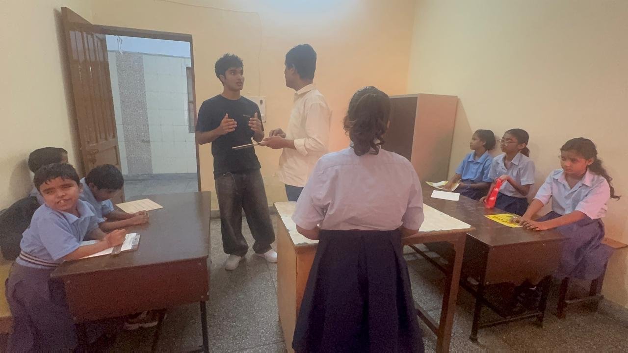 In discussion with a teacher while students sit at their desks in the classroom
