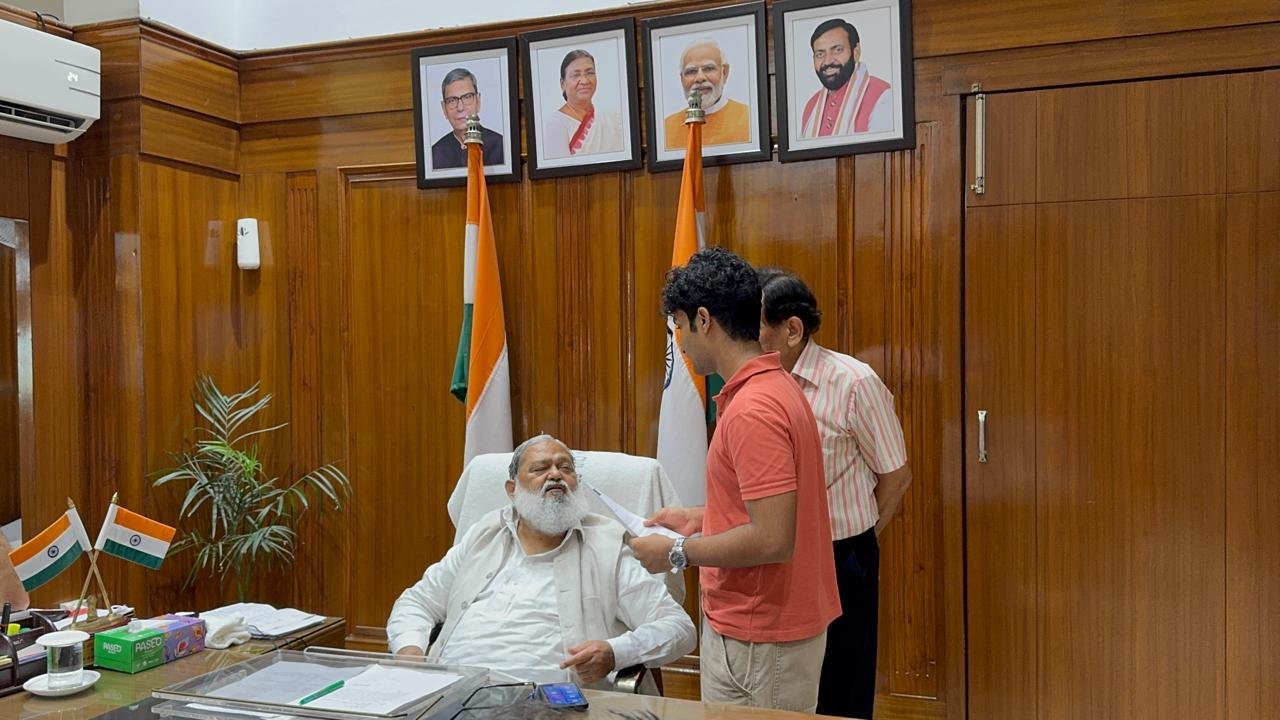 Anil Vij signing the petition as officials and a police officer stand by, with snacks laid out on the desk