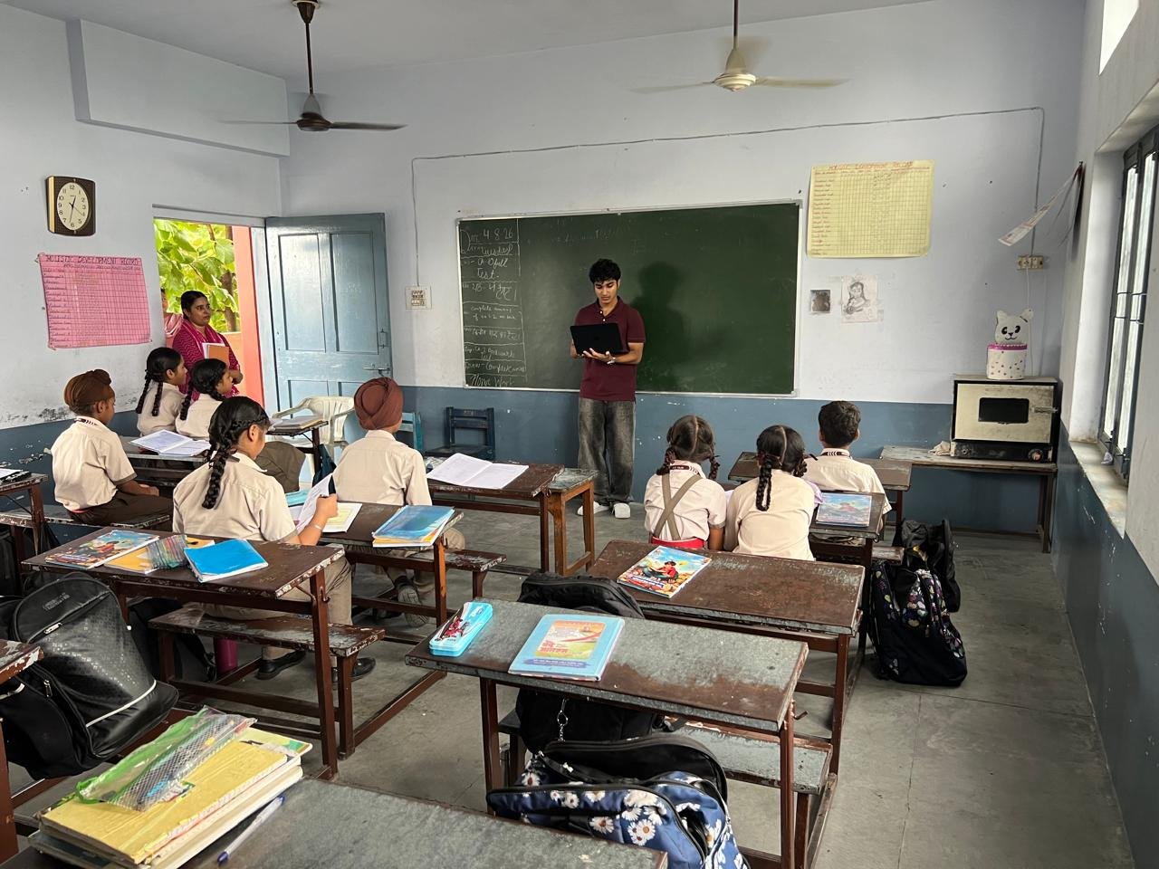 Leading a workshop from the front of the classroom, laptop in hand, as students follow along