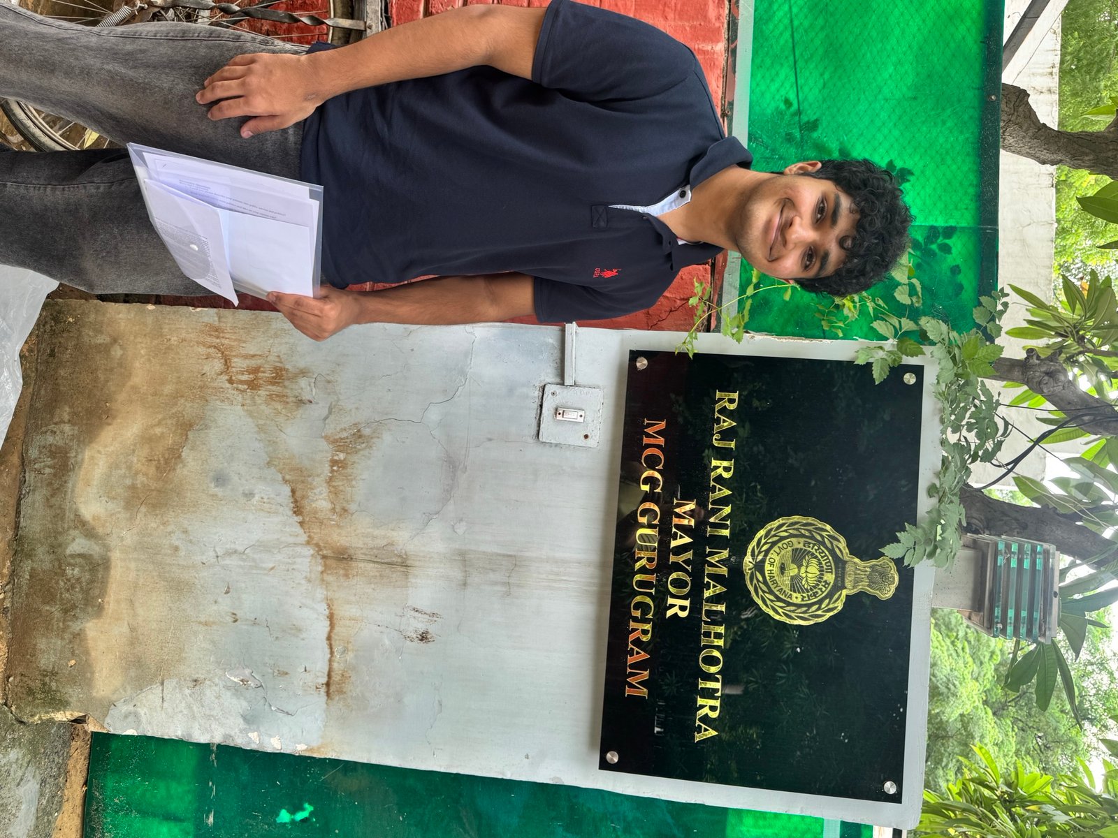 Standing outside the Municipal Corporation of Gurugram beside the sign reading Raj Rani Malhotra, Mayor, MCG Gurugram
