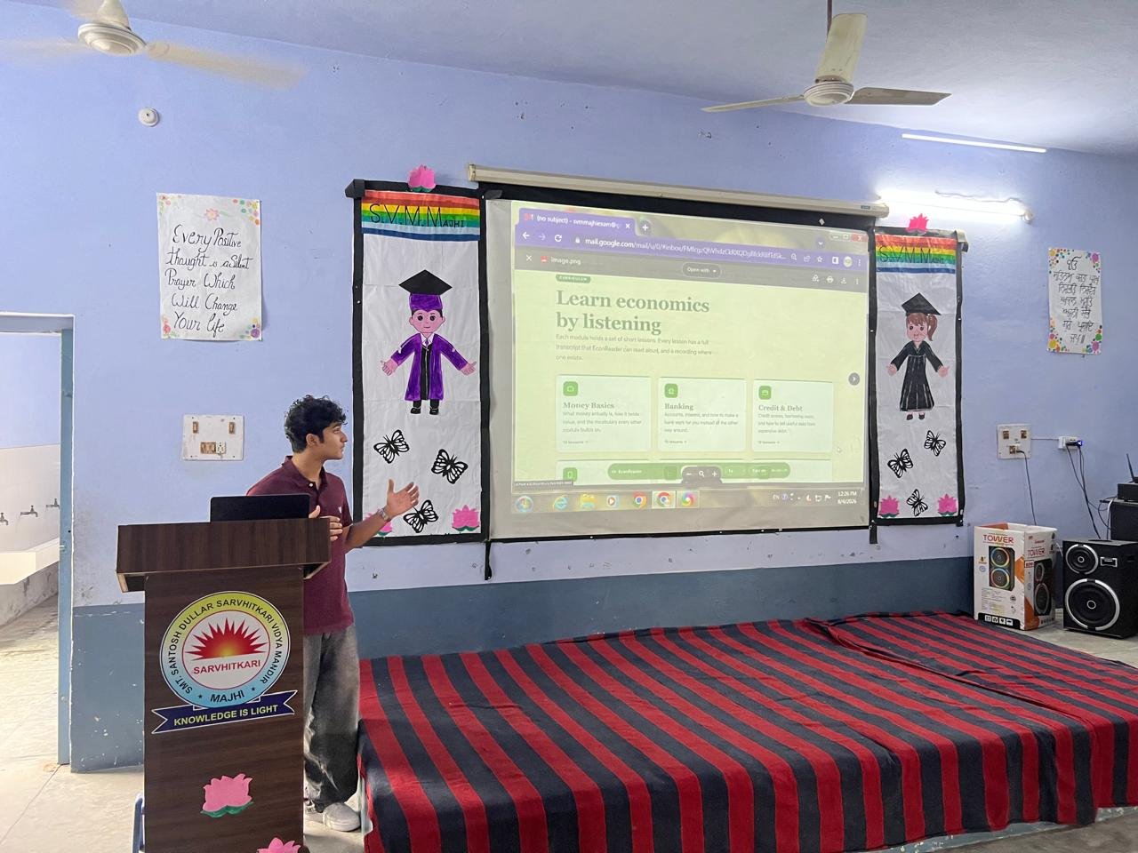 Presenting the EconReads curriculum to students from behind a podium, with the 'Learn economics by listening' slide projected on screen